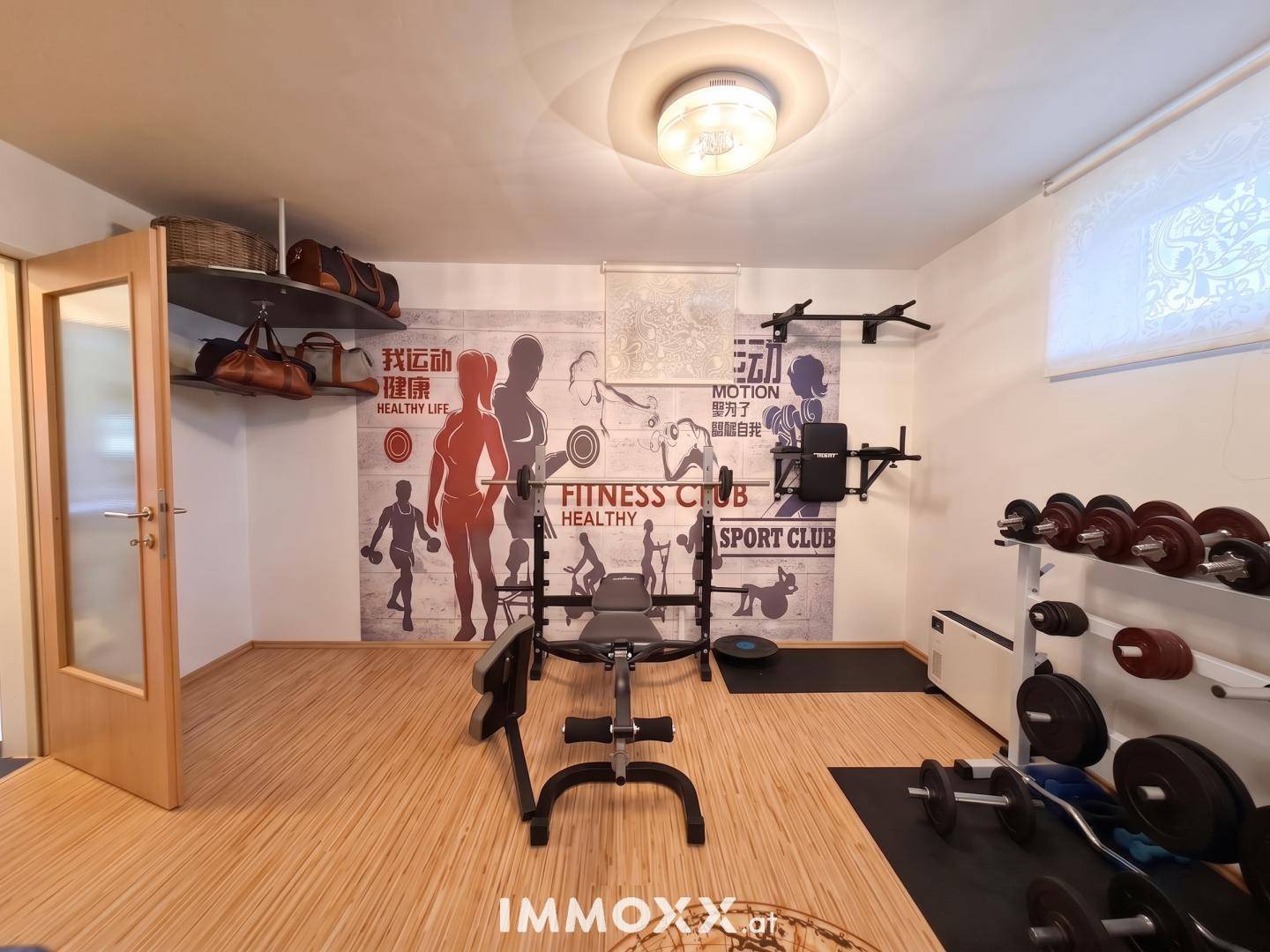 Fitnessraum im Untergeschoss mit Trainingsgeräten, Gewichten und einer motivierenden Wandgestaltung.