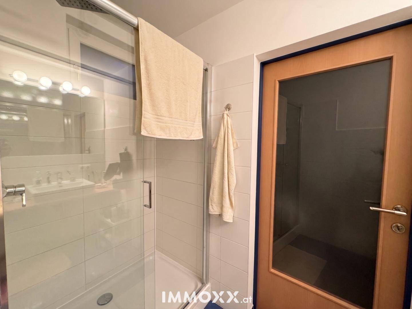 Duschbereich im Badezimmer mit Glasabtrennung, weißen Fliesen und einer Milchglastür.