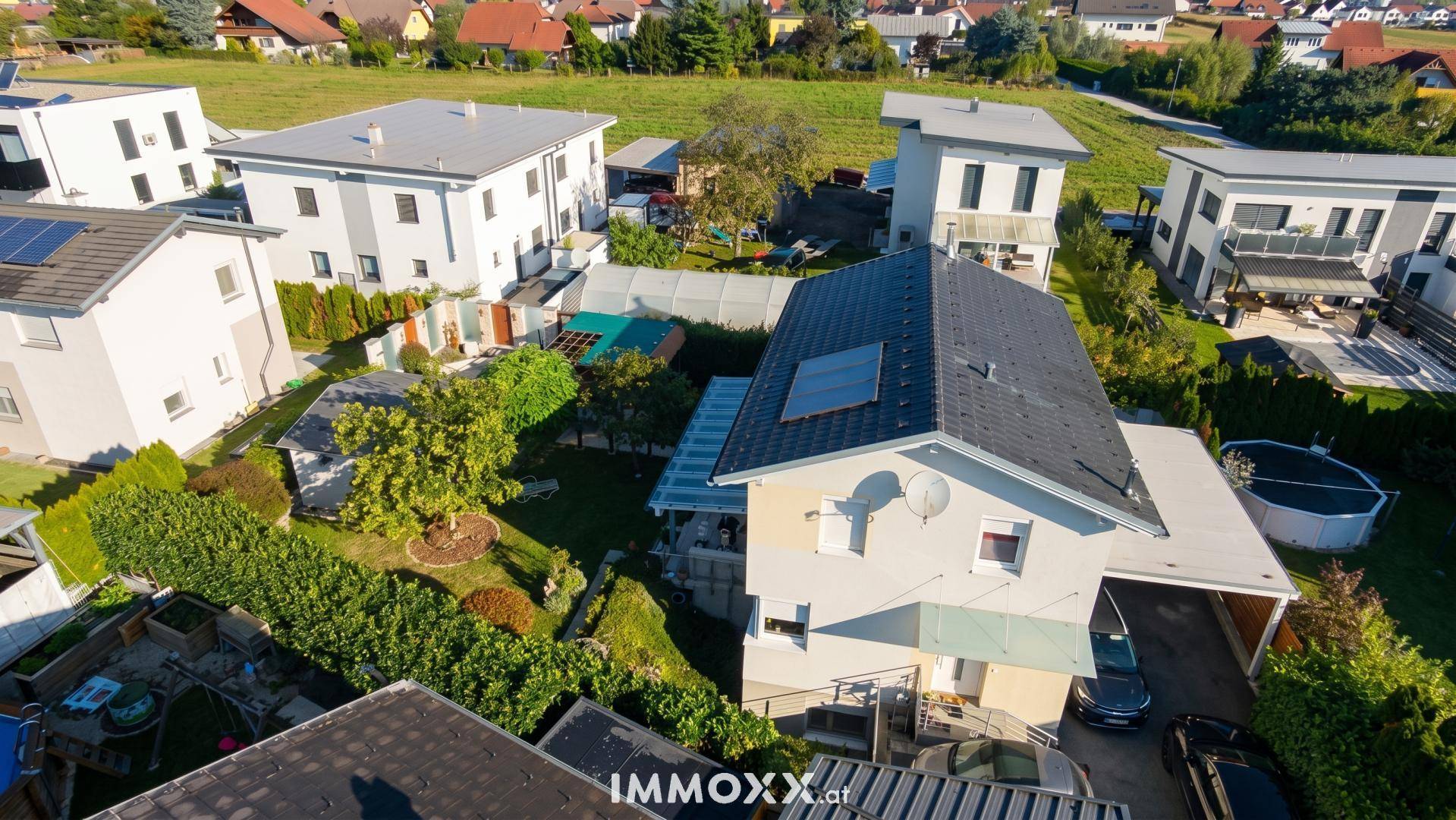 Luftaufnahme eines Einfamilienhauses mit Solaranlage, Carport und gepflegtem Garten in ländlicher Umgebung.