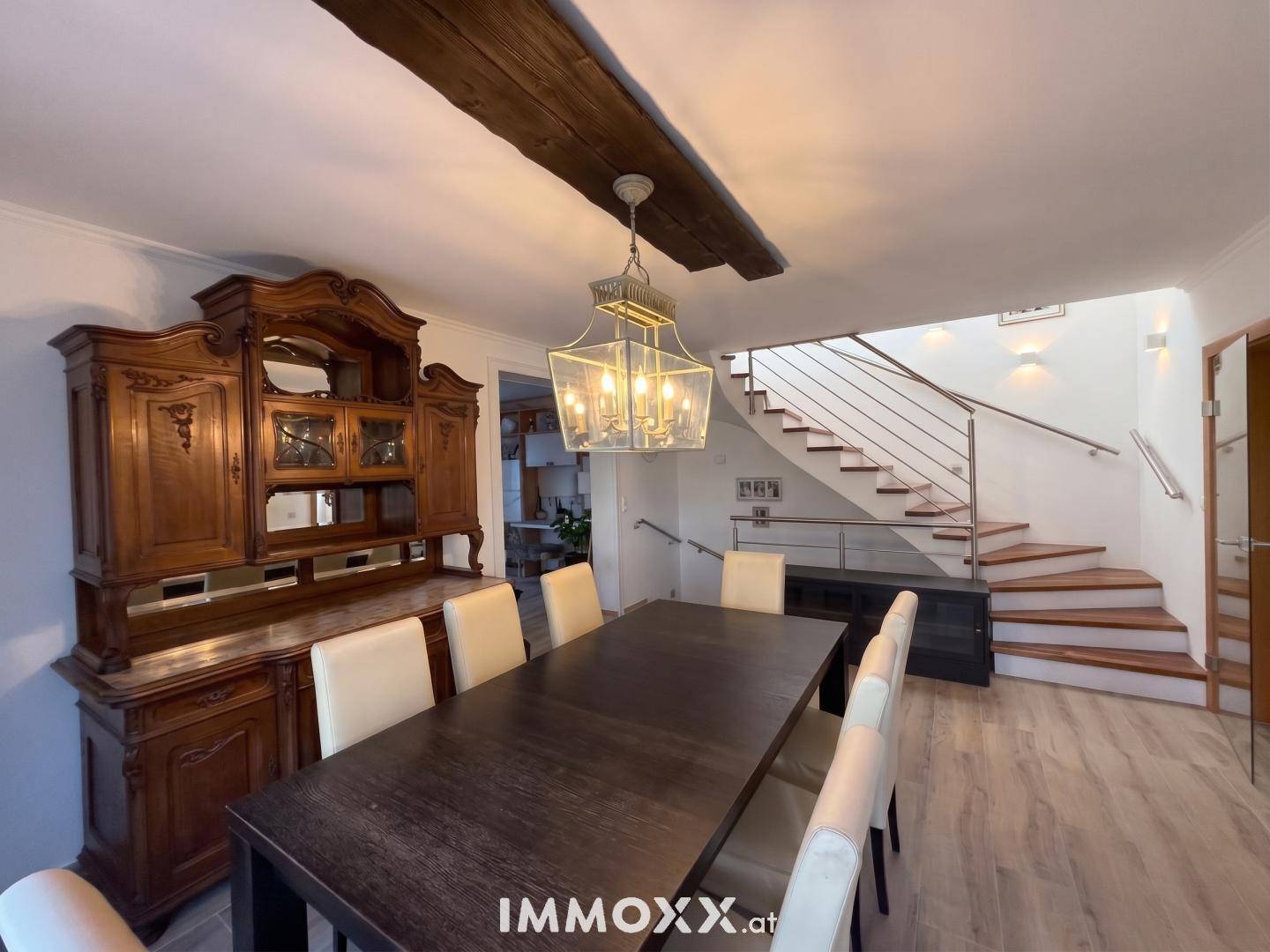 Eleganter Essbereich mit großem Holztisch, antiker Anrichte und einer modernen Treppe ins Obergeschoss.