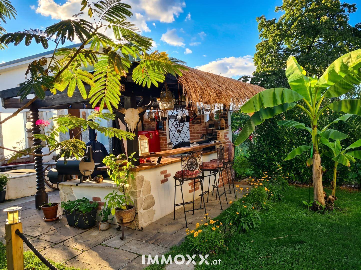 Exotische Außenbar mit Strohdach, umgeben von üppiger tropischer Vegetation und Palmen.