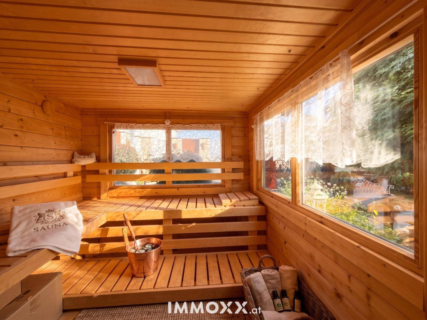 Gemütlicher Saunaraum aus Holz mit Sitzbänken und großen Fenstern für natürliche Belichtung.