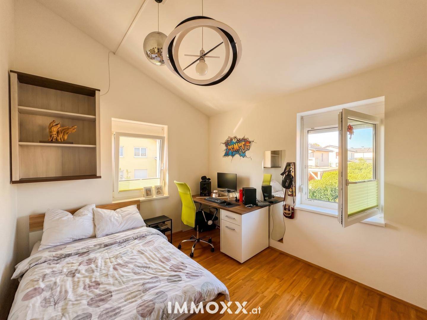 Helles Schlafzimmer oder Arbeitszimmer mit Bett, Schreibtisch und zwei Fenstern.