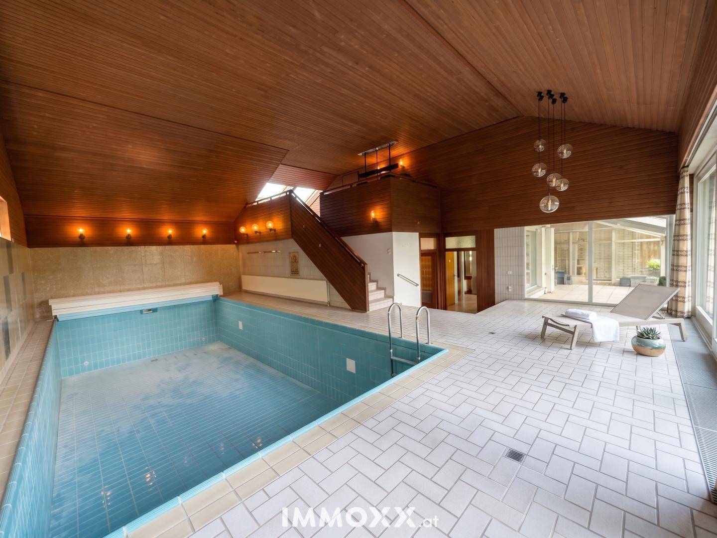 Großer Innenpoolbereich mit Holzdecke, gefliestem Boden und einer Treppe zum oberen Bereich.