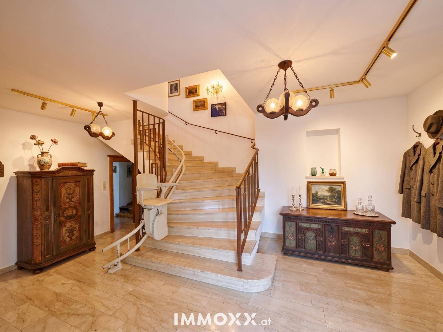 Geräumiger Flur mit eleganter Marmorboden, geschwungener Treppe und einem Treppenlift für Barrierefreiheit.