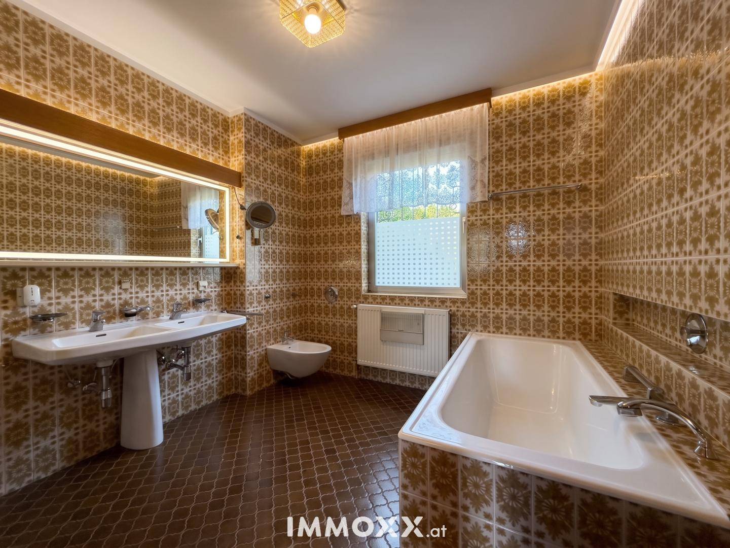 Badezimmer im Stil der 80er Jahre mit braunen Fliesen, Badewanne, Bidet und Doppelwaschbecken.