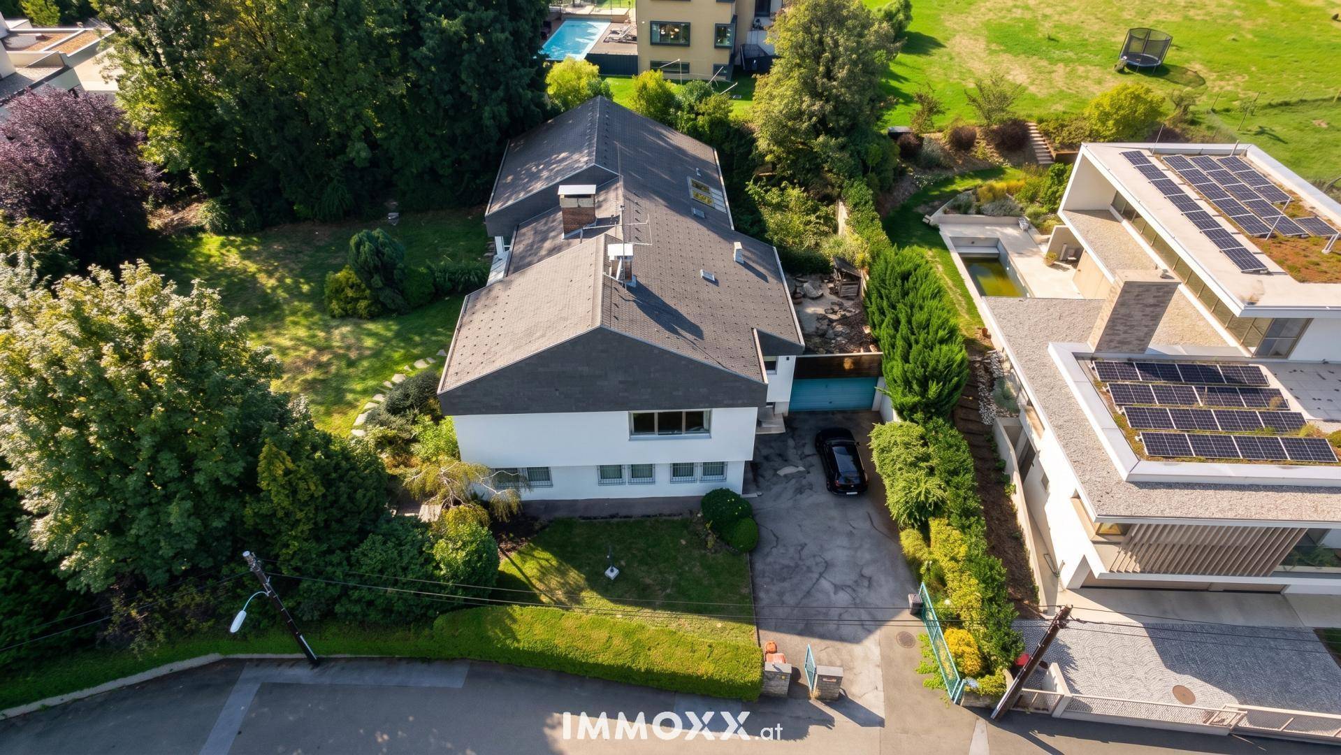 Luftaufnahme des Hauses mit umliegendem Garten und benachbarten modernen Gebäuden mit Solaranlagen.