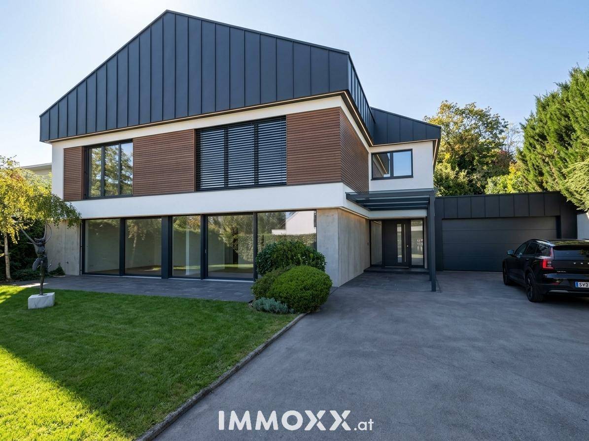 Moderne Hausfassade mit dunklem Metalldach, großen Fenstern und einer gepflegten Auffahrt.