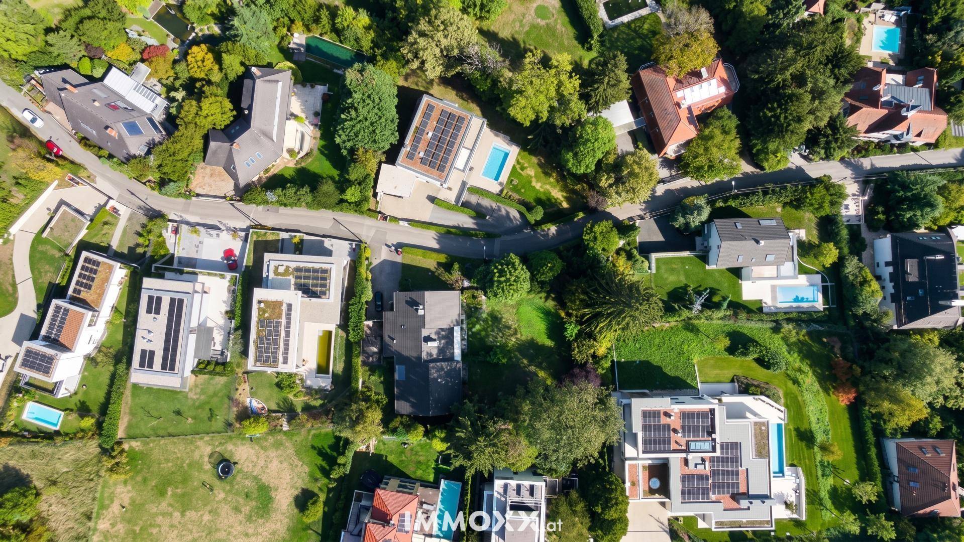 Vogelperspektive einer Wohnsiedlung mit modernen Häusern, Pools und Solaranlagen auf den Dächern.