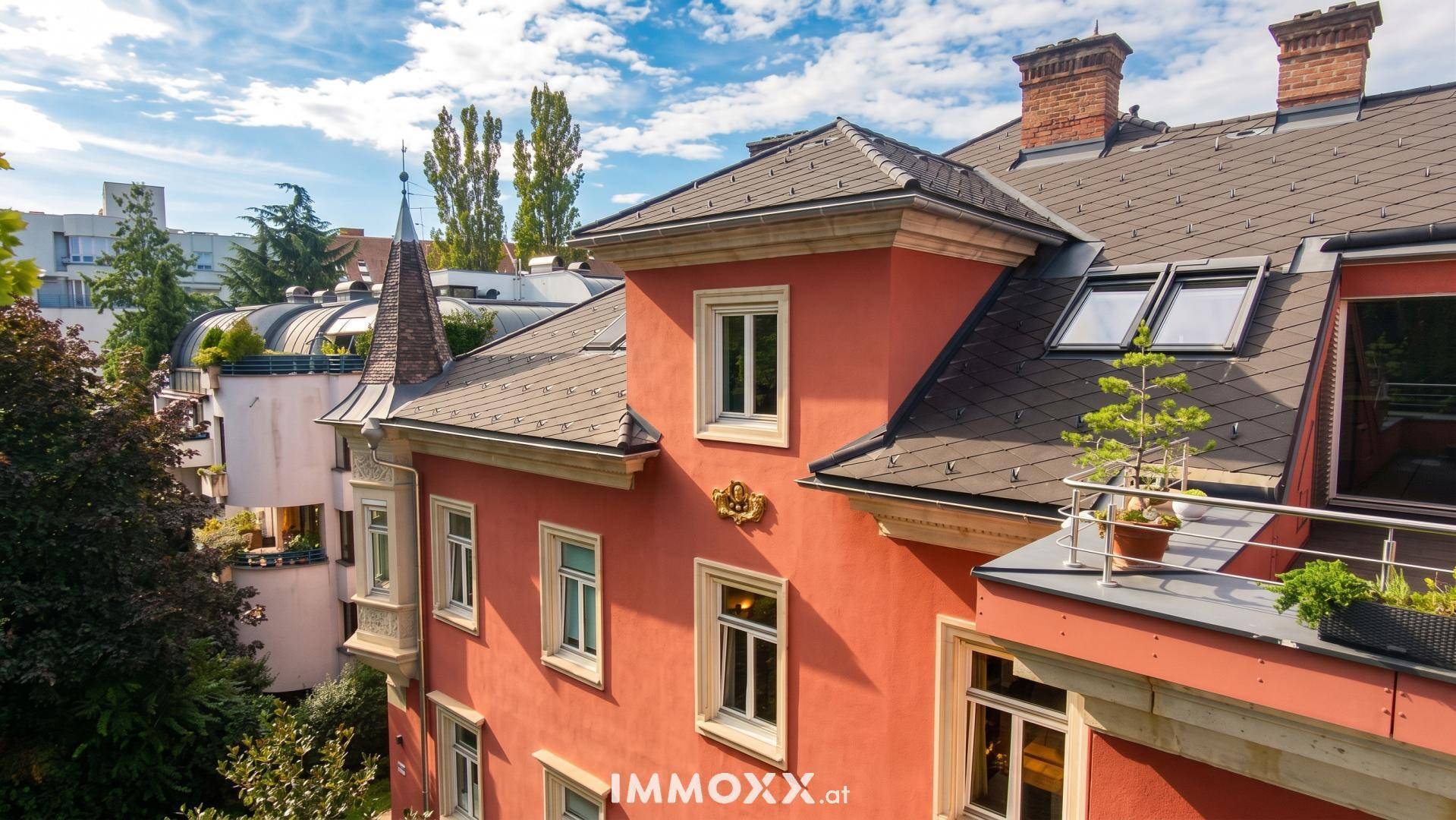 Nahaufnahme der roten Gebäudefassade mit Fenstern, einem kleinen Balkon und traditionellen Schornsteinen.