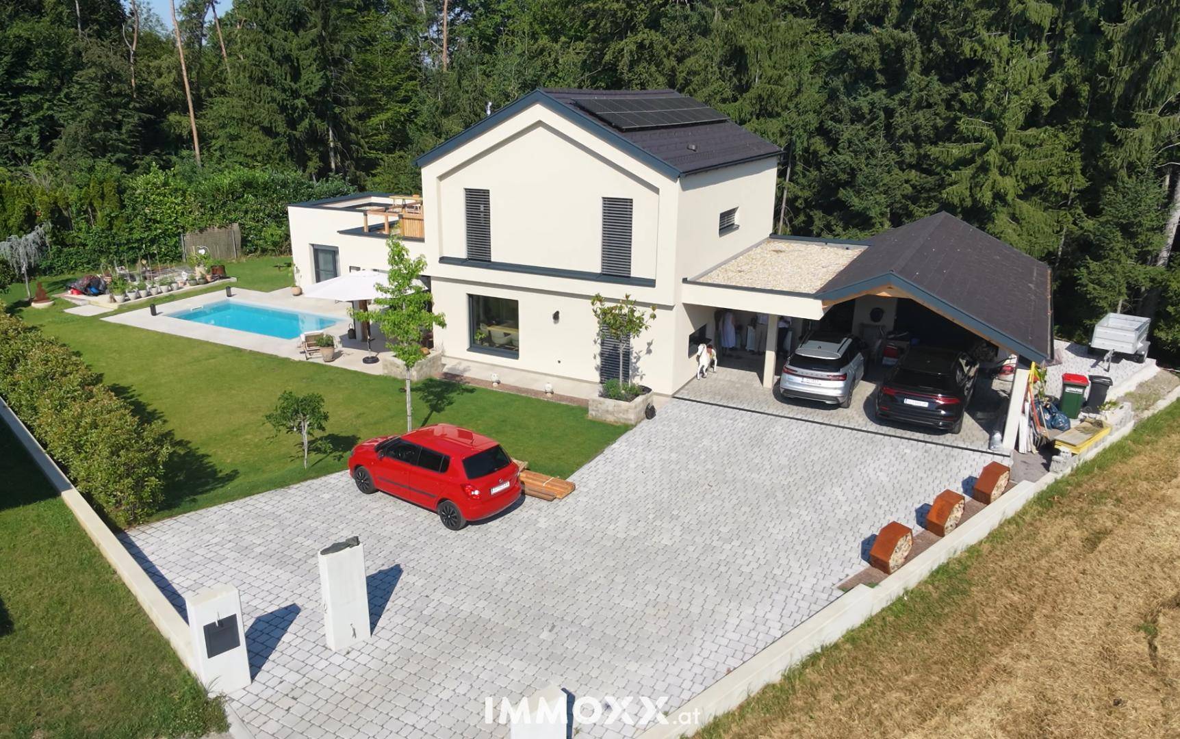 Gesamtansicht des modernen Hauses mit großem Garten, Poolbereich und Carport umgeben von Bäumen.
