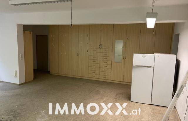 Innenansicht eines gewerblichen Raumes mit Einbauschränken, einem Kühlschrank und Betonboden.