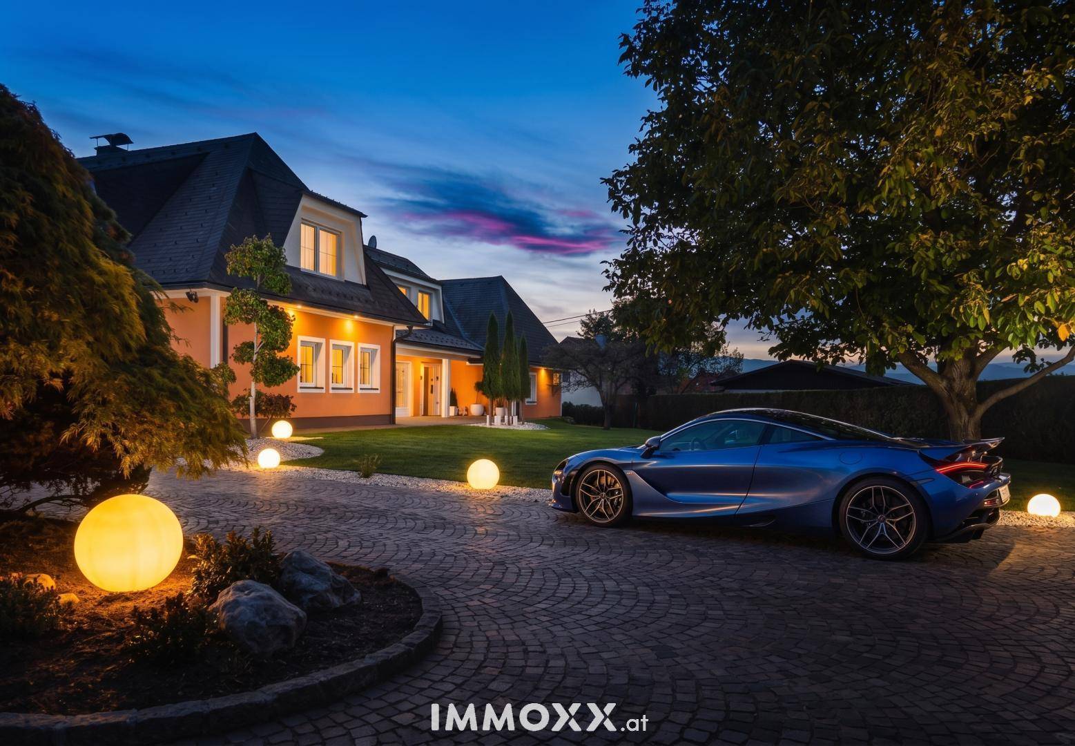 Elegantes Haus bei Sonnenuntergang mit beleuchteter Auffahrt und gepflegtem Vorgarten.
