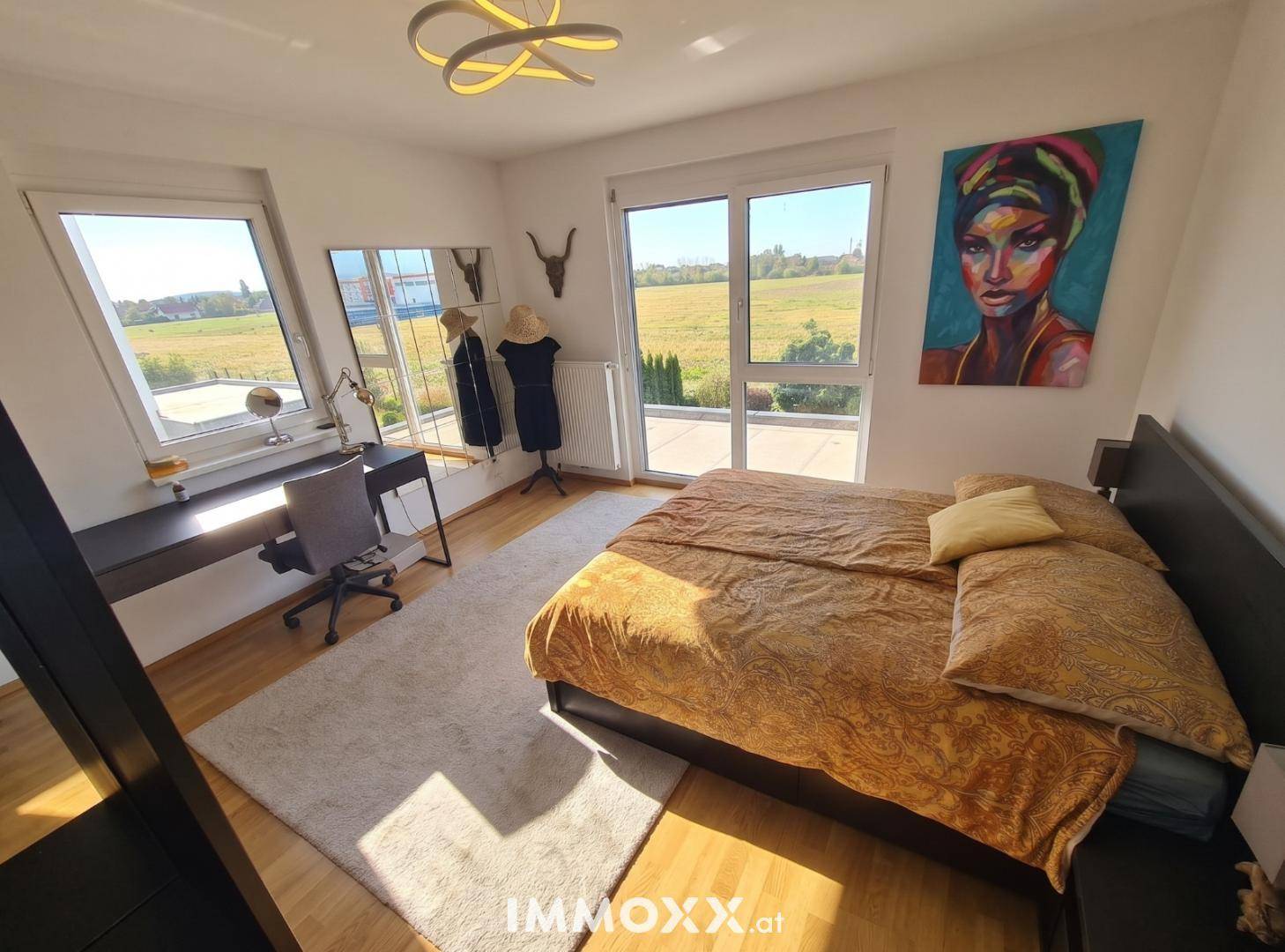 Helles Schlafzimmer mit Holzboden, großem Fenster und Zugang zu einem Balkon oder Terrasse.