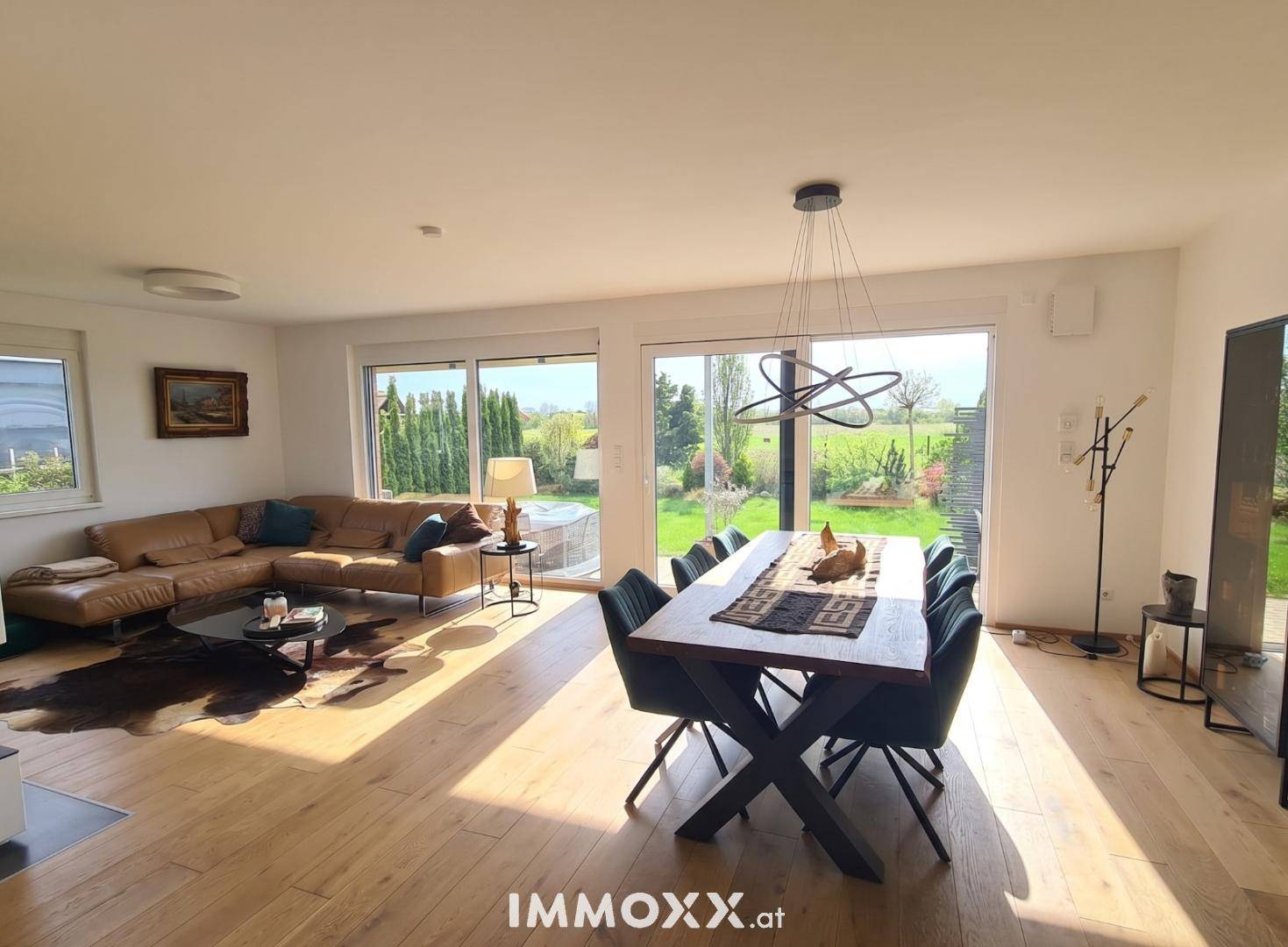 Helles, offenes Wohn-Esszimmer mit Holzboden, großzügigen Fenstern und Blick ins Grüne.