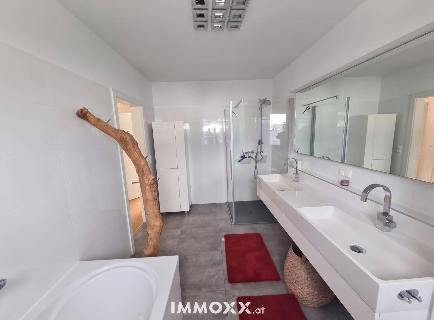Modernes Badezimmer mit Doppelwaschbecken, Badewanne, Dusche und großen Fliesen.
