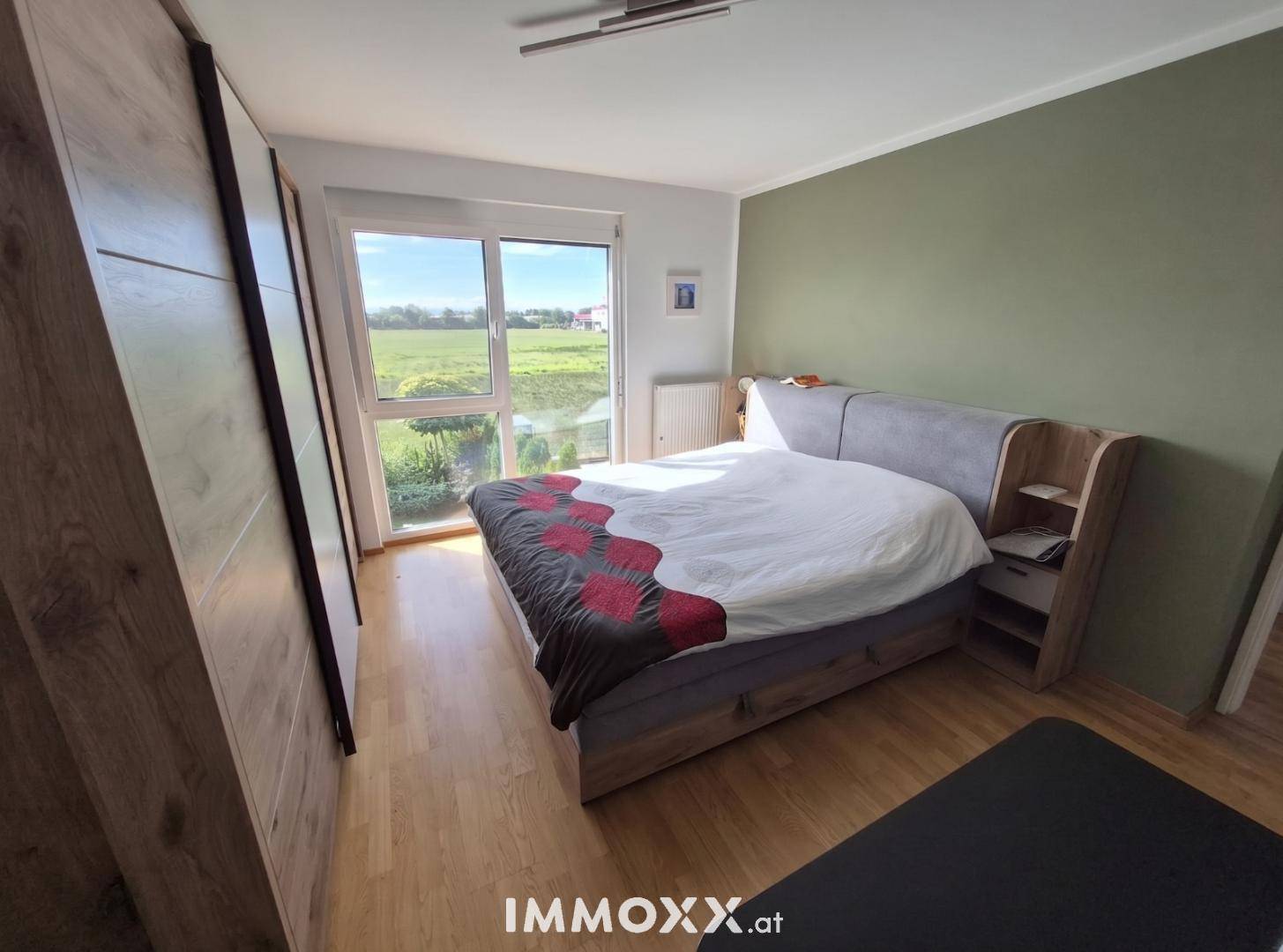 Gemütliches Schlafzimmer mit Holzboden, großem Fenster und Blick ins Grüne.