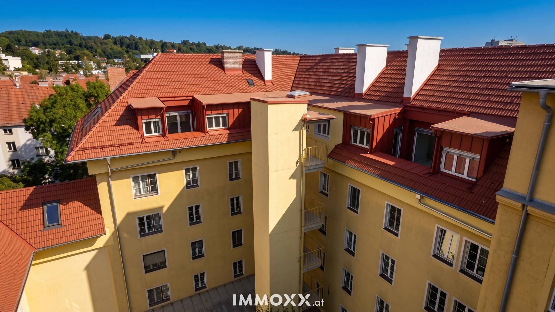 Gelbes Wohngebäude mit roten Ziegeldächern und einem Innenhof unter strahlend blauem Himmel.