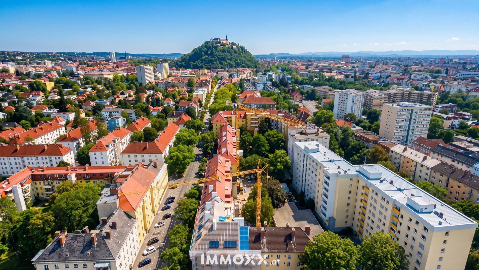 Weitläufige Luftaufnahme einer Stadt mit vielen Wohngebäuden, Grünflächen und einem Hügel im Hintergrund.