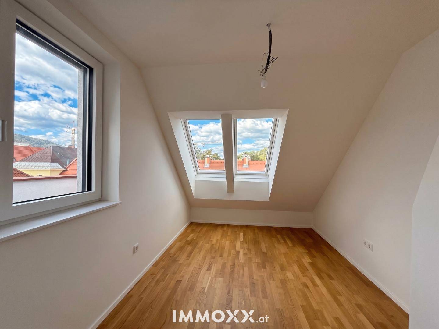 Helles Zimmer im Dachgeschoss mit Holzboden und zwei großen Dachfenstern.