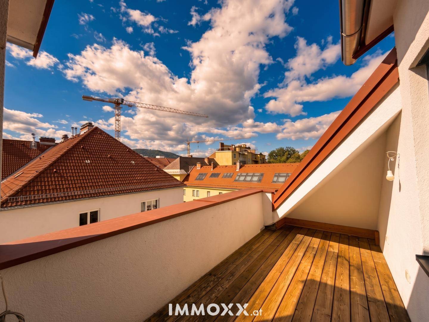 Kleiner Balkon mit Holzboden und Blick über die Dächer der Stadt.