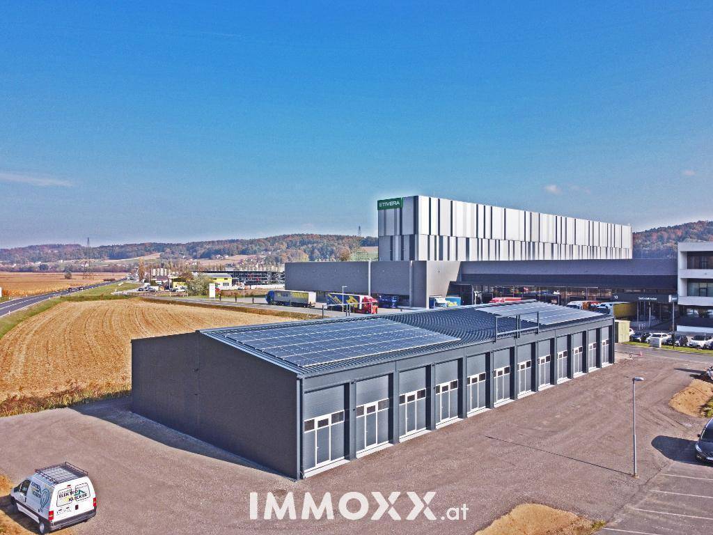 Luftaufnahme des Gewerbegebäudes mit Solaranlage auf dem Dach und umliegender Infrastruktur.