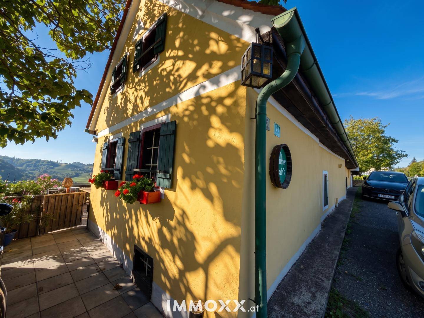 Traditionelles gelbes Gebäude mit grünen Fensterläden und bunten Blumenkästen unter strahlendem Sonnenschein.