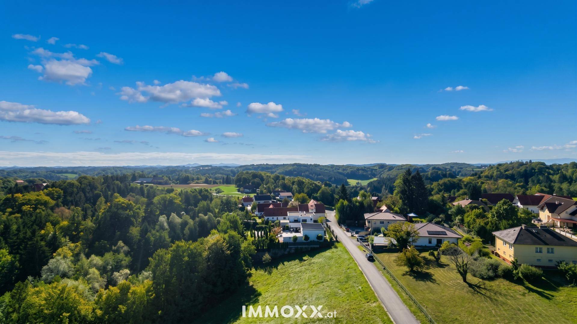 Luftaufnahme einer weitläufigen grünen Landschaft mit Wohnsiedlungen und einem klaren blauen Himmel.