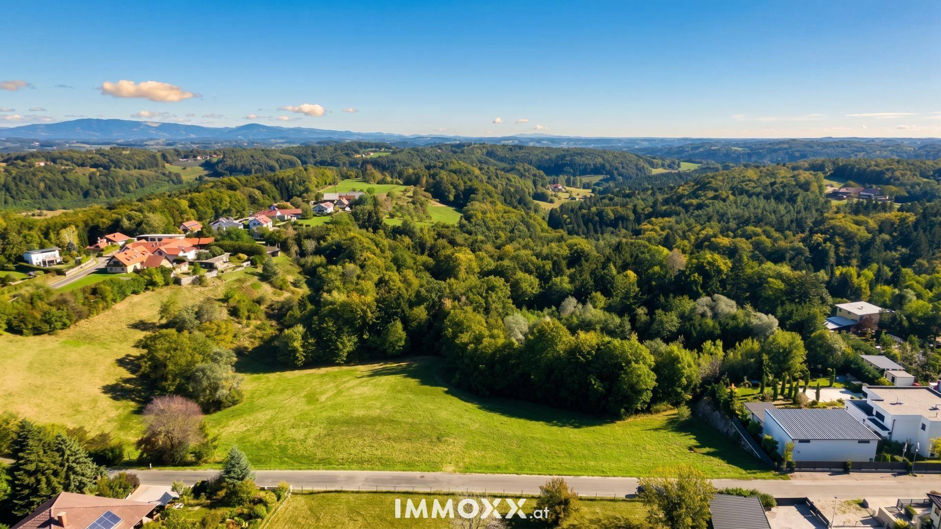 Weitläufiger Blick über eine grüne Hügellandschaft mit verstreuten Häusern und Bergen am Horizont.