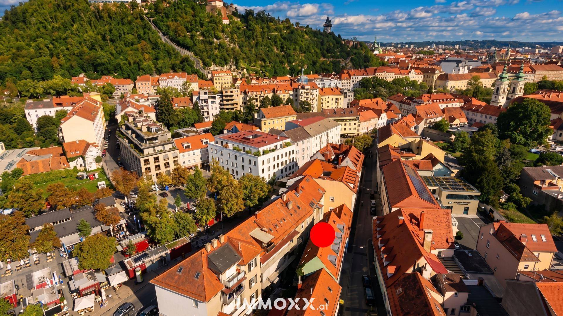 Weitläufige Luftaufnahme einer historischen Stadt mit grünen Hügeln und roten Dächern.