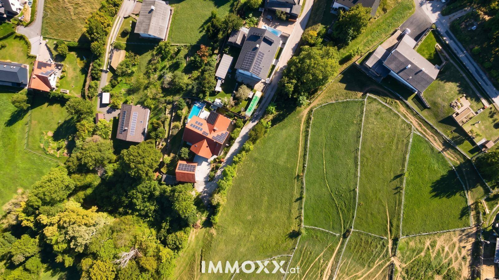 Luftaufnahme eines Wohngebiets mit Häusern, grünen Feldern und einem Pool auf einem Grundstück.
