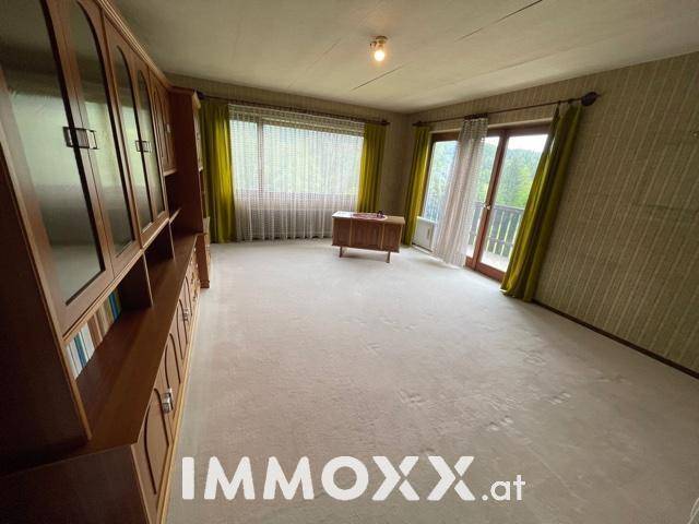 Gemütliches Wohnzimmer mit Teppichboden, Holzschrank und Zugang zum Balkon.