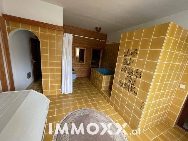 Großes Badezimmer mit gelben Fliesen, Sauna und kleiner Badewanne.