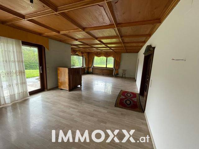 Geräumiger Wohnbereich mit Holzdecke, Parkettboden und großen Fenstern zum Garten.