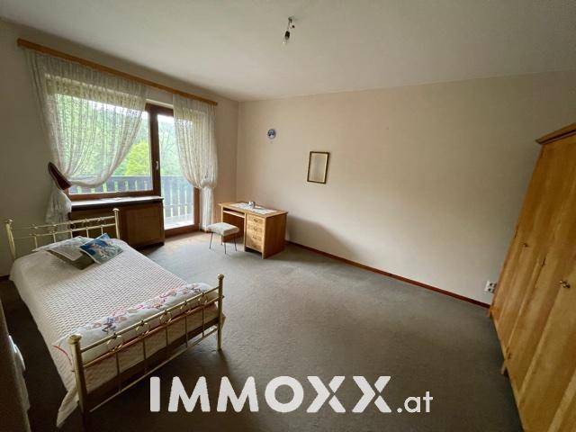 Schlafzimmer mit Teppichboden, Schreibtisch und Zugang zu einem kleinen Balkon.
