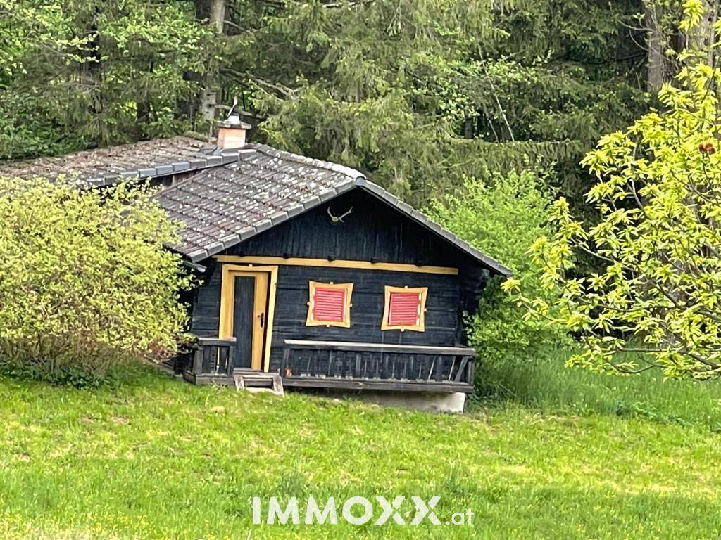Rustikale Holzhütte mit rotem Fensterladen und traditionellem Dach in grüner Umgebung.