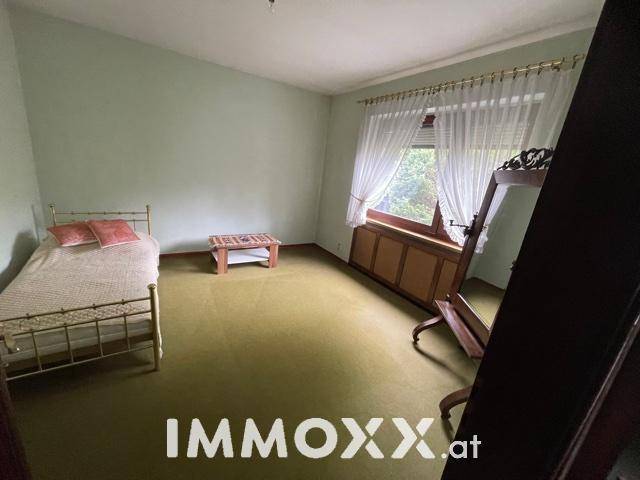 Schlafzimmer mit grünem Teppichboden, Einzelbett und großem Spiegel.