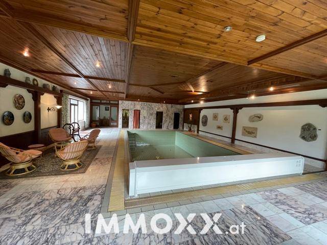 Geräumiger Innenpoolbereich mit Marmorboden, Holzdecke und Sitzgelegenheiten.