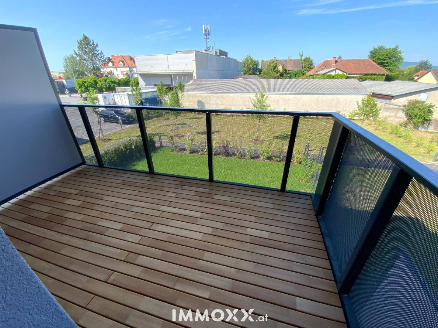 Sonniger Balkon mit Holzdielen und Blick auf die umliegende Nachbarschaft.