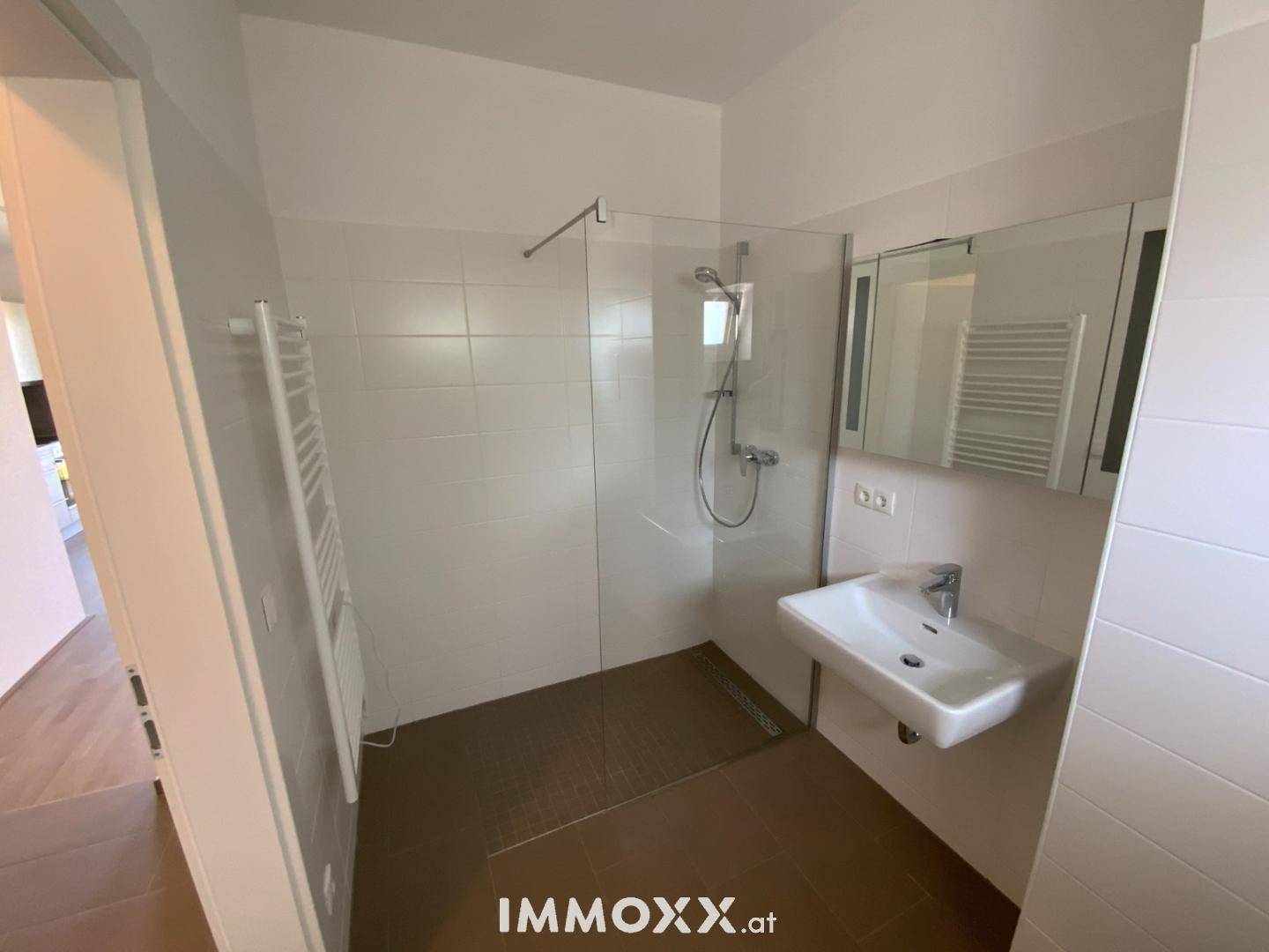 Modernes Badezimmer mit ebenerdiger Dusche, Waschbecken und beheiztem Handtuchhalter.