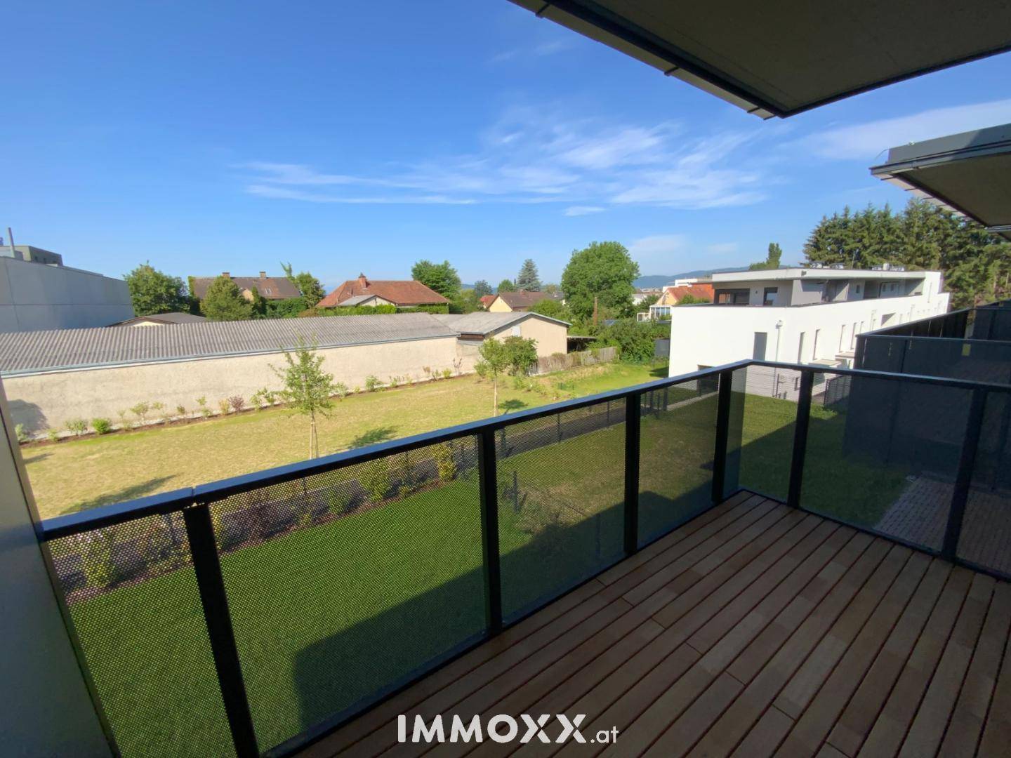 Geräumiger Balkon mit Holzboden, Glasgeländer und Blick ins Grüne.