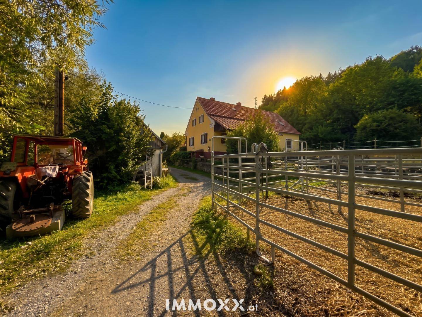 Landhaus in ländlicher Umgebung bei Sonnenuntergang mit einem Traktor im Vordergrund.