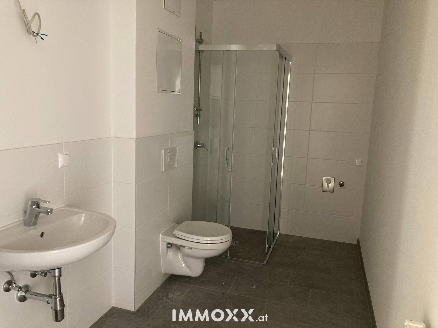 Modernes Badezimmer mit weißen Fliesen, dunklem Fliesenboden, wandhängendem WC und einer Duschkabine.