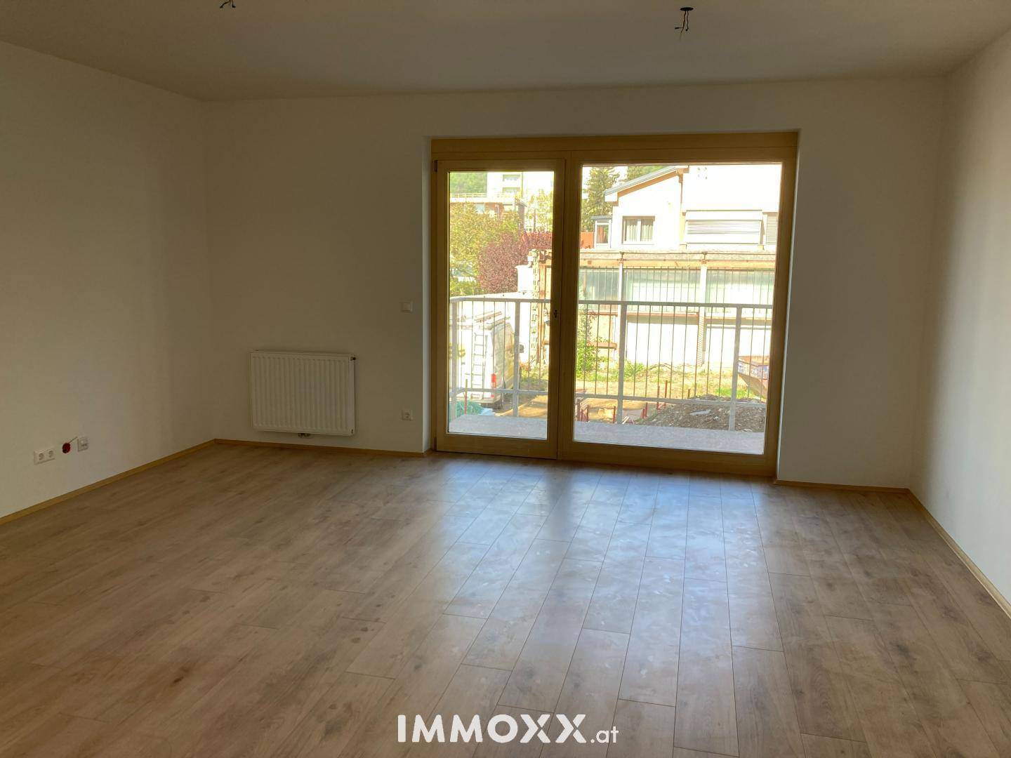 Heller, leerer Raum mit Laminatboden, weißen Wänden und großem Zugang zu einem Balkon oder einer Terrasse.