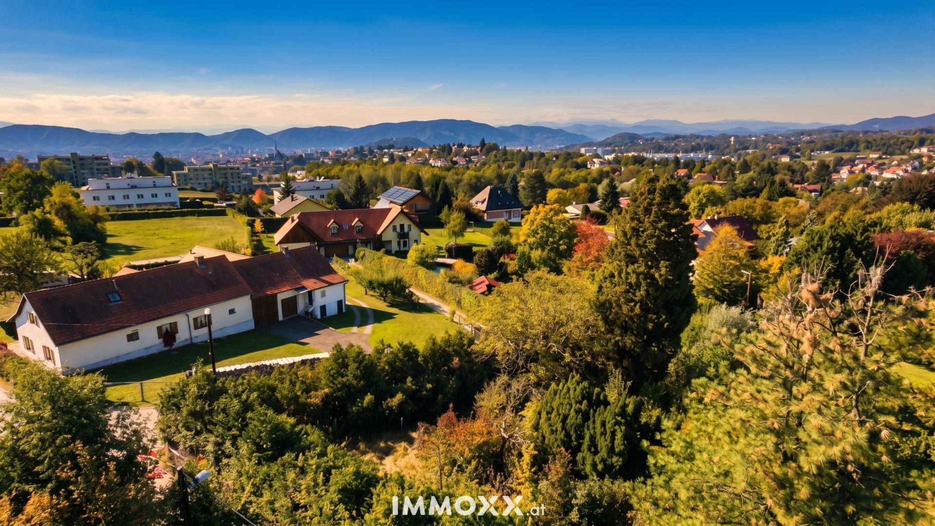 Weitläufige Luftaufnahme einer ländlichen Wohngegend mit grünen Hügeln und Bergen am Horizont.