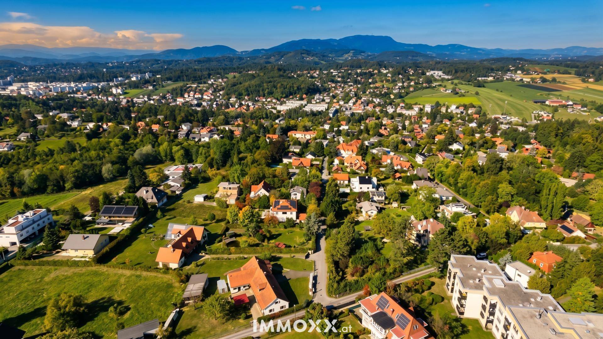 Breite Luftaufnahme einer Wohngegend mit vielen Bäumen, Häusern und einer malerischen Bergkulisse.