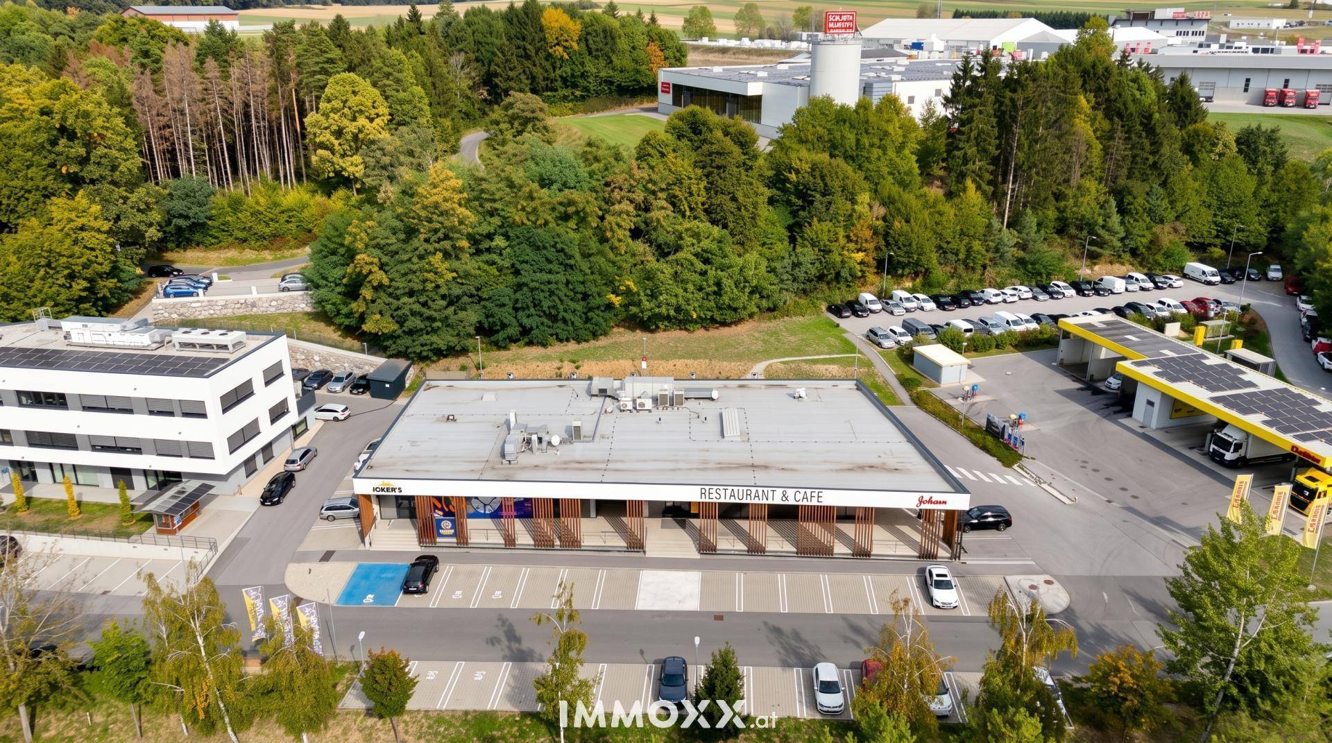 Luftaufnahme eines Restaurants und Cafés mit großem Parkplatz und umliegenden Bäumen und Solaranlagen.