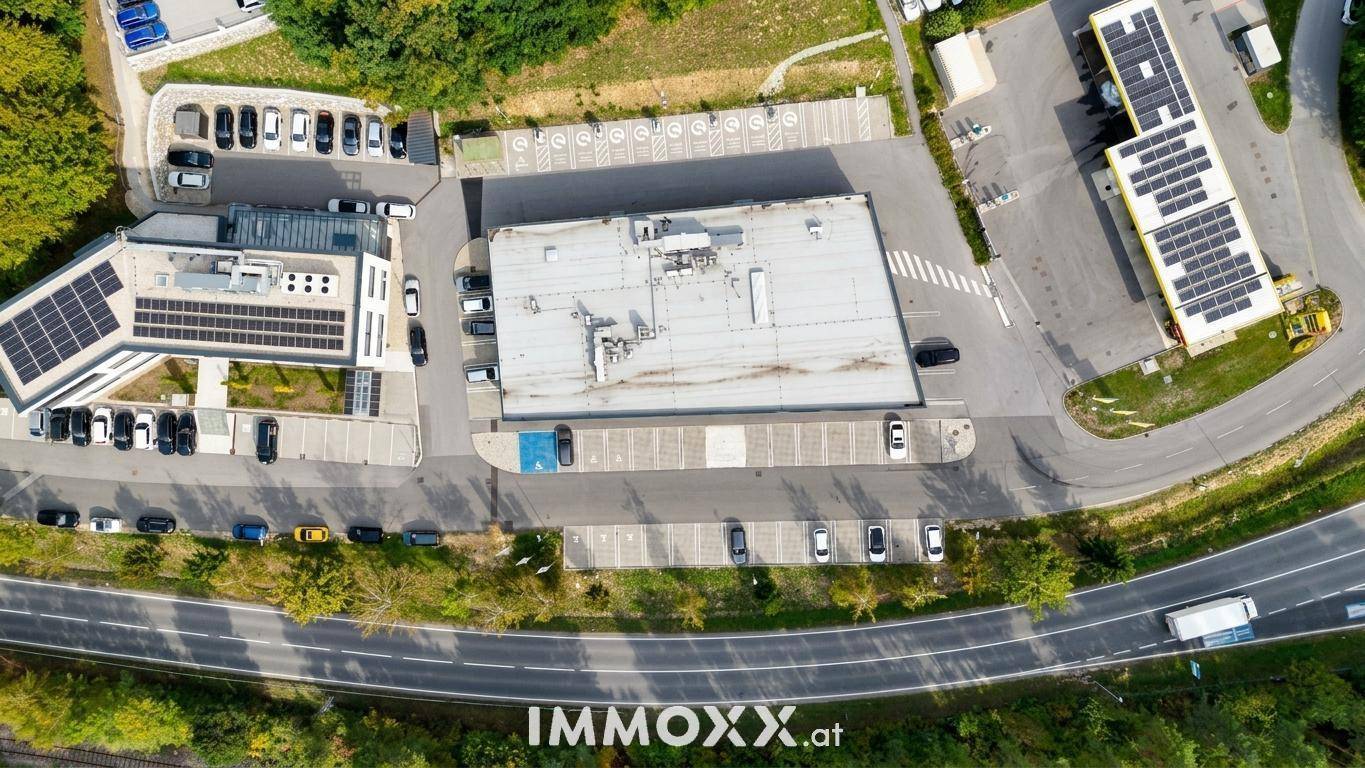 Senkrechte Luftaufnahme von Gewerbegebäuden mit Parkplätzen, Straßeninfrastruktur und Solaranlagen auf Dächern.