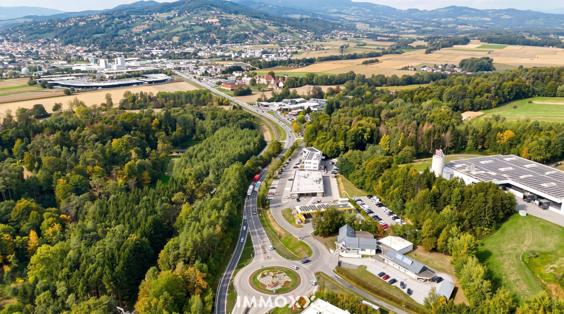 Weitläufige Luftaufnahme einer Gewerbefläche mit Straßennetz, Wald und einer Stadt in der Ferne.