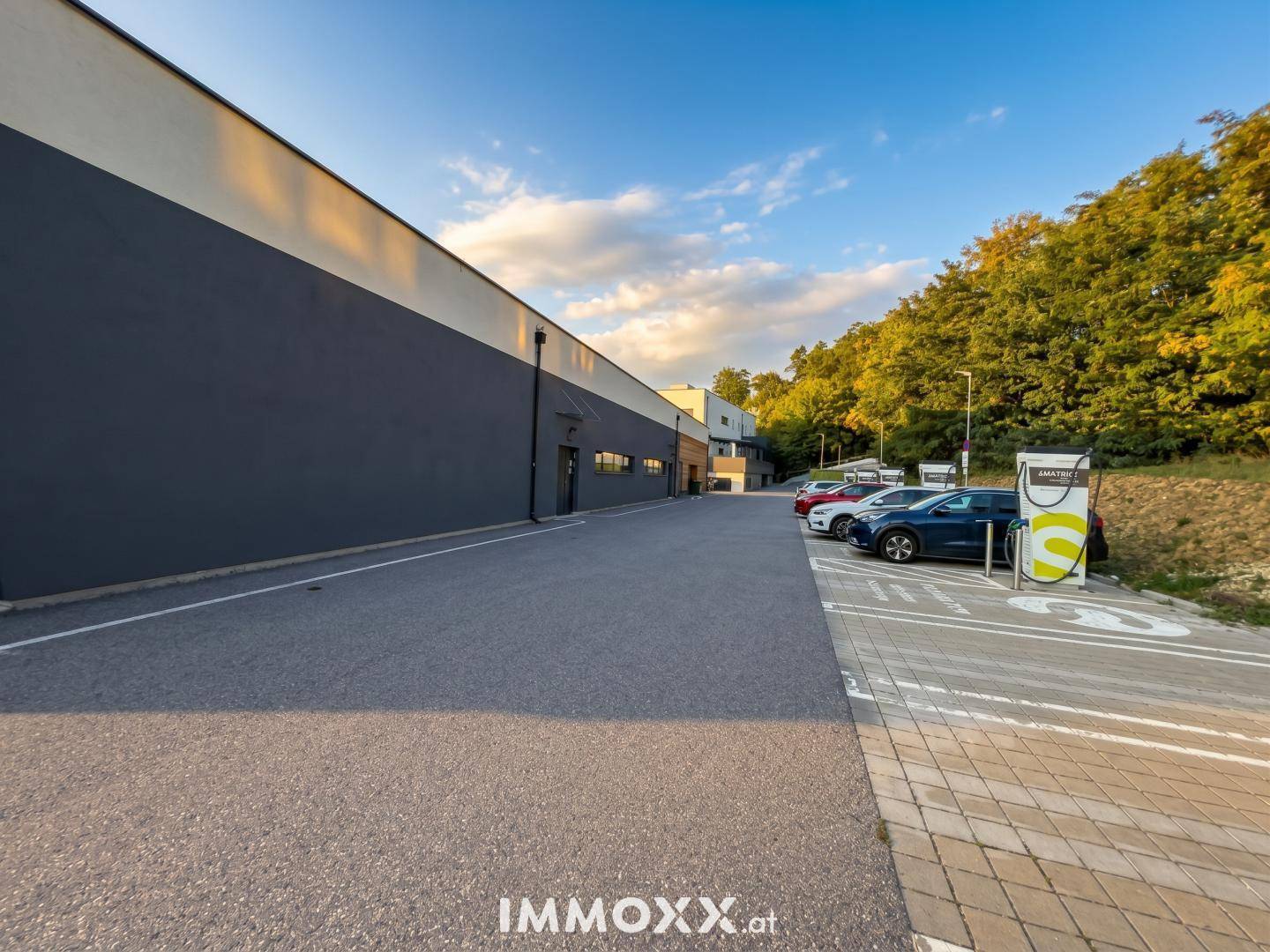 Außenansicht eines Geschäftsgebäudes mit großem Parkplatz und Ladestationen für Elektrofahrzeuge bei Sonnenuntergang.